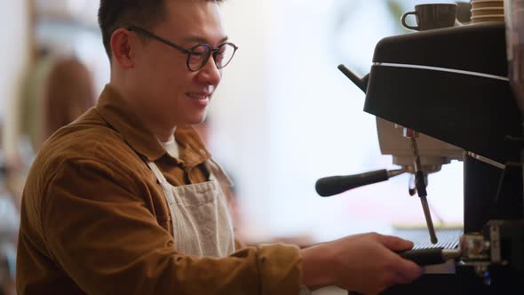 Smiling Asian man barista brews coffee