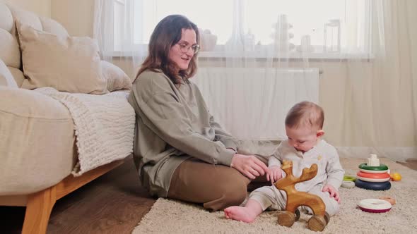 A happy child and mother play with a wooden moose toy on the carpet in the home room, age 8 months.