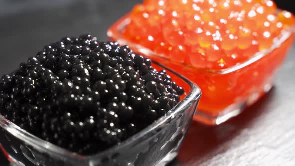 Red and Black Caviar in Two Identical Transparent Glass Bowls on a Black Background