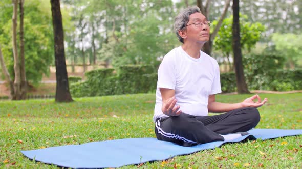 Senior man in lotus pose sitting on green grass in a park. Concept of calm and meditation.