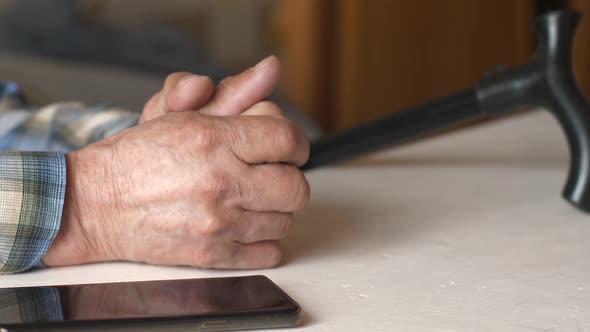 Elderly man lonely waiting for a phone call in depression theme. Close-up of a pensioner's hands, a 