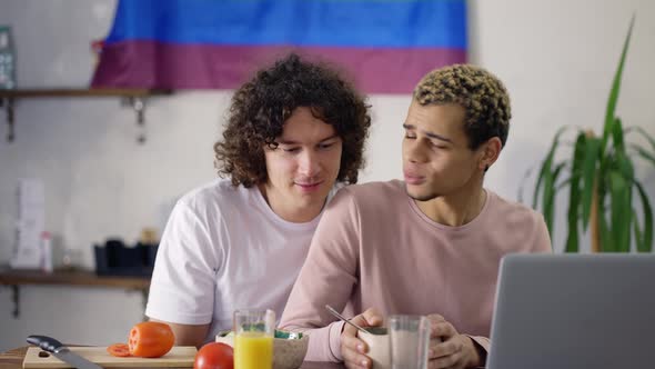 Pretty Couple Gay on the Kitchen Together During Breakfast Watching News on Laptop
