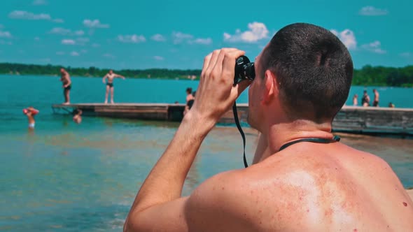 Man on the Beach in Swimming Trunks is Watching Someone Through Binoculars