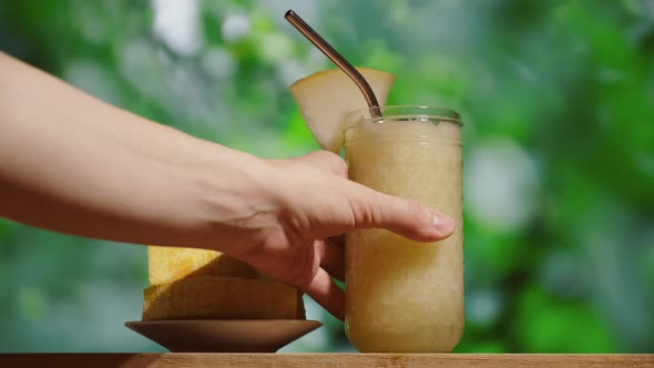 Female Hand Puts Glass of Melon Smoothie on Table Bar