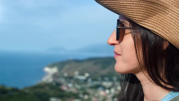 Face of Happy Smiling Young Female Tourist in Sunglasses and Hat Relaxing at Beautiful Sea Landscape