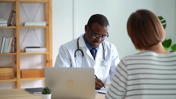 Male Doctor Therapist Writing and Talking with Female Patient at Table in Clinic Spbas