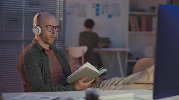Man in Headphones Reading at Workplace at Night