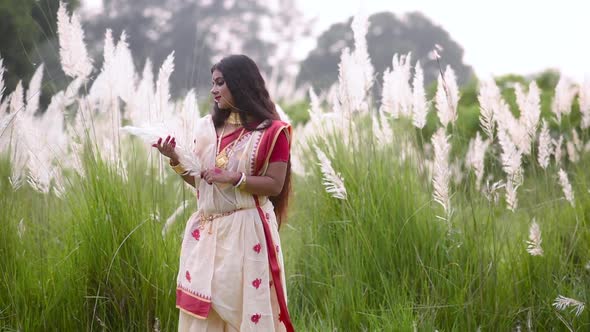 A calm and beautiful Indian woman is happy and plays with white grass called saccharum spontaneum in