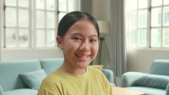 Close Up Of Asian Kid Girl Sitting In A Wheelchair Smiling And Looking At Camera In Living Room