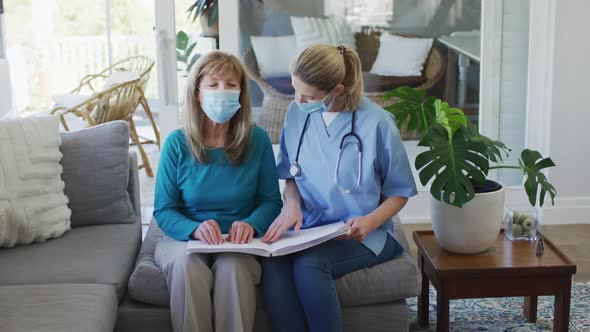 Female health worker assisting senior woman to read braille book