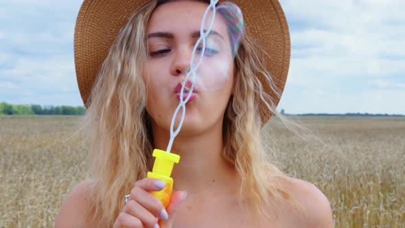 A Woman Blows Soap Bubbles Next to a Cereal Field