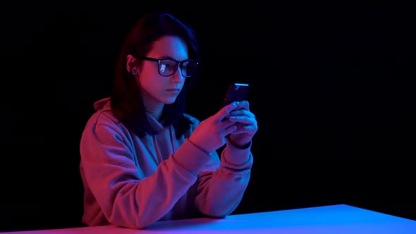 Young Woman with a Smartphone. Woman Use the Phone. Blue and Red Light Falls on a Woman on a Black