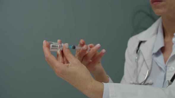 Closeup of Hands Holding Vial Filling Syringe with Vaccine Indoors