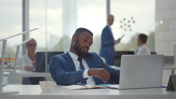 Tired Young African Manager Working on Laptop Sitting at Desk in Office