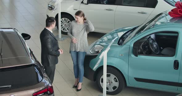 Top View of Young Beautiful Caucasian Woman Talking with Car Dealer in Showroom. Positive Successful