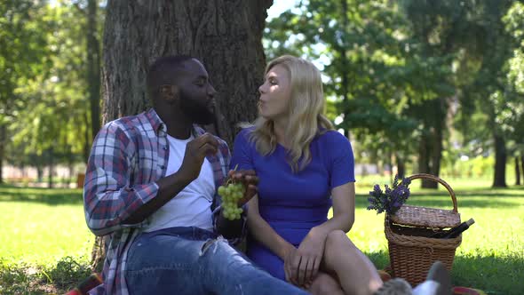 Mixed Race Couple Eating Grapes in Park and Speaking, Spending Time Together