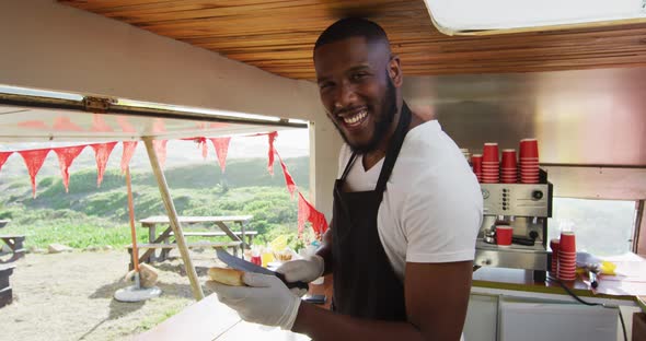 Portrait of african american man smiling while preparing hot dogs in the food truck