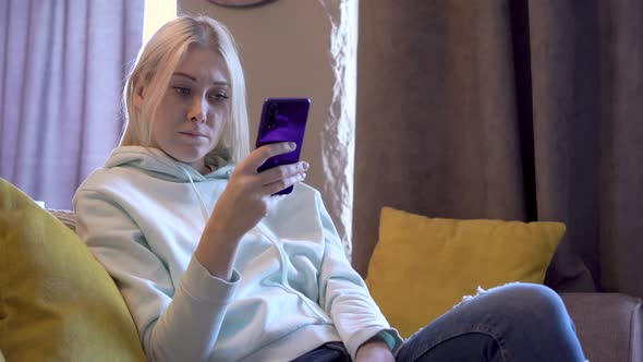 Young female user using mobile phone while sitting on sofa at home.