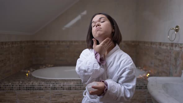 Confident Little Woman Applying Moisturizer on Neck Skin Standing in Bathroom Indoors