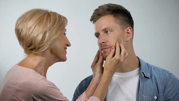 Smiling Mother Pinching Irritated Son Cheeks, Adult Child Care, Overprotection