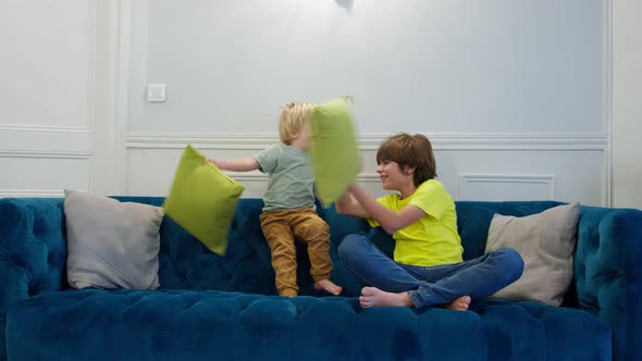 Blond Boy and His Brother Fight with Pillows Sitting on Couch