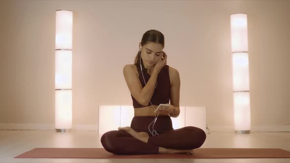 Woman in Earphones Listening Music on Smartphone. Woman Meditating in Studio