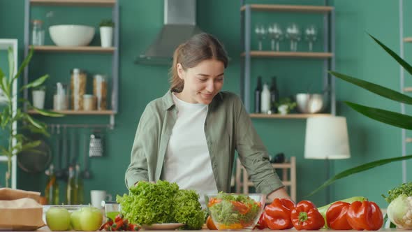 Happy Young Woman Preparing Healthy Food Using Organic Products in the Kitchen at Home