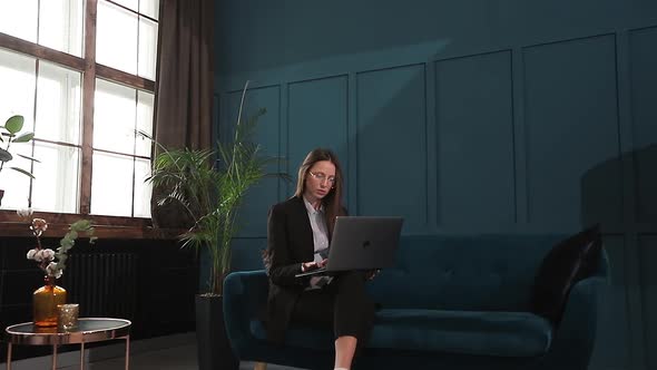 Portrait of an Elegant Businesswoman Sitting with Laptop on the Couch at the Luxury Blue Office