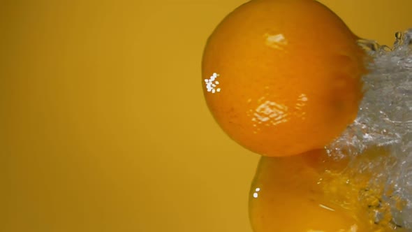 Oranges are Bouncing Horizontally with Water Splashes on the Yellow Background
