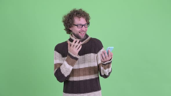 Happy Young Bearded Man Using Phone and Looking Surprised