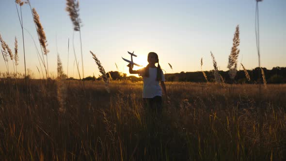 Happy Small Girl Walking with Airplane Through Grass Field