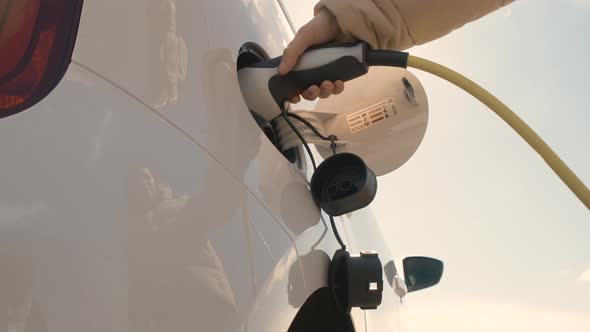 Bottom View of Woman Hand Disconnect a Power Cable Supply to Charge Electric or EV Car at Sunlight