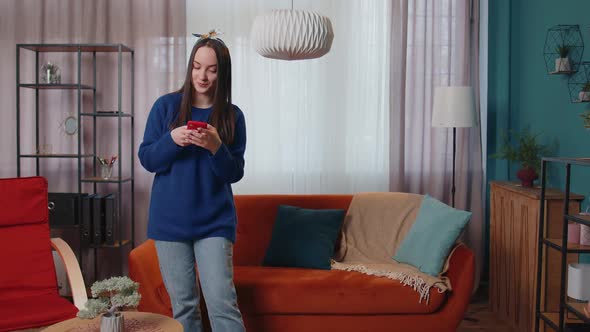 Relaxed Smiling Caucasian Young Woman Standing at Home with Smartphone Scrolling Browsing Online