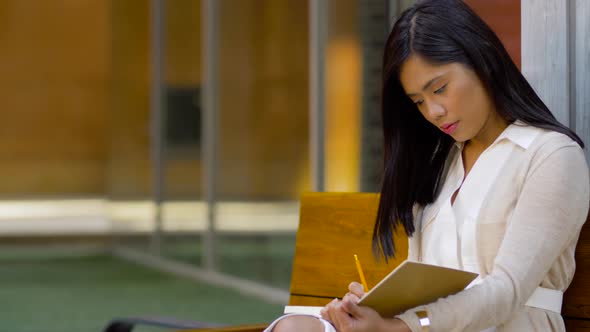 Asian Woman with Notebook or Sketchbook on Bench