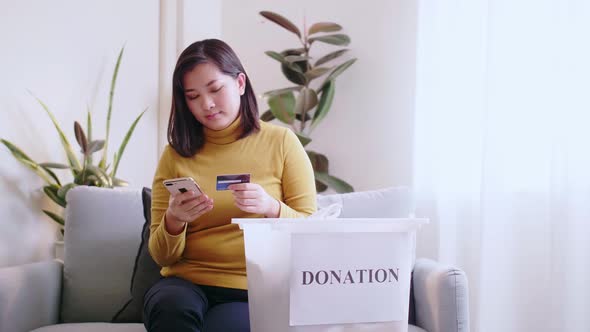 Woman pressing phone using a credit card to pay online to reserve donation box delivery. Concept cam