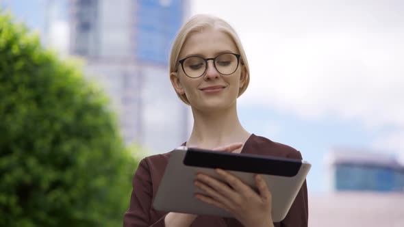 Young Cheerful Woman in Glasses Scrolls the Tablet and Watches the News Feed on Social Networks on