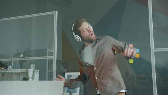 Playful Employee Attractive Man Wearing Headphones Dancing in Glass Wall Office