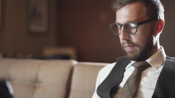 Young Businessman in Glasses Working at a Laptop Man in the Suit Sitting on the Couch in the Hotel