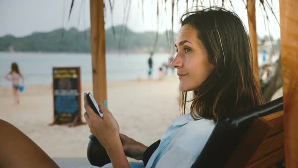 Side View Shot of Young Happy Smiling Tourist Woman with Drink and Smartphone Resting