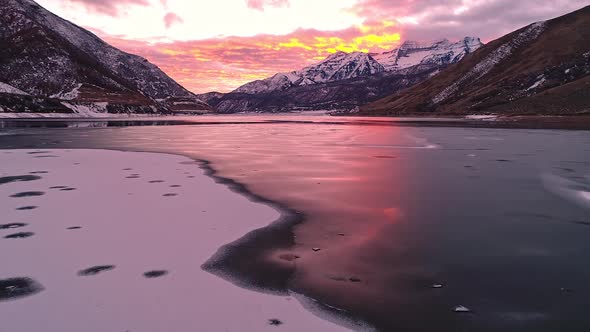 Flying over lines of ice and snow on frozen lake during colorful sunset