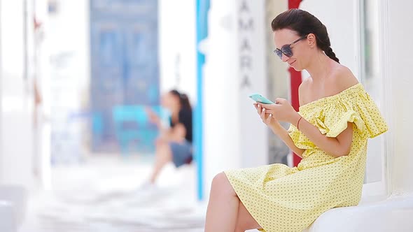 Beautiful Woman with Smart Phone Outdoors in Old Streets an Mykonos. Girl at Street of Typical Greek