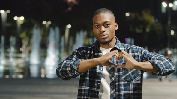 Friendly Kind African American Young Man Guy Shows Shape of Heart with Hands Fingers Looks Inside