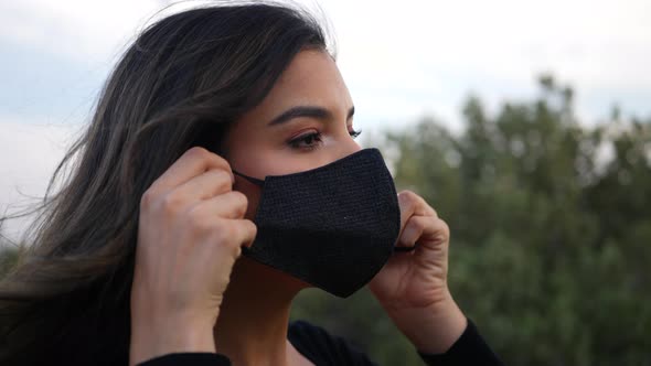 Attractive hispanic woman putting on a reusable cloth respiratory face mask to prevent infection fro