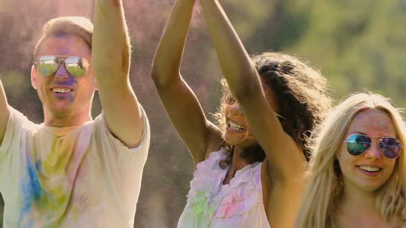 Happy Best Friends Dancing and Jumping in Colorful Dust Clouds at Holi Festival