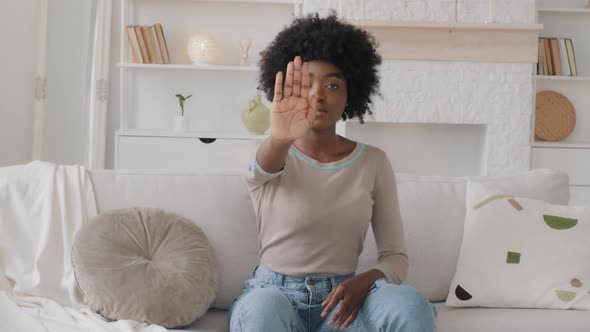 Young Serious African Woman Sitting on Sofa Looking at Camera Outstretched Her Palm to Cam Closeup