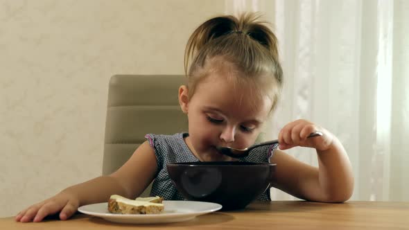 Preschool girl sitting at a table eats soup. Close-up.