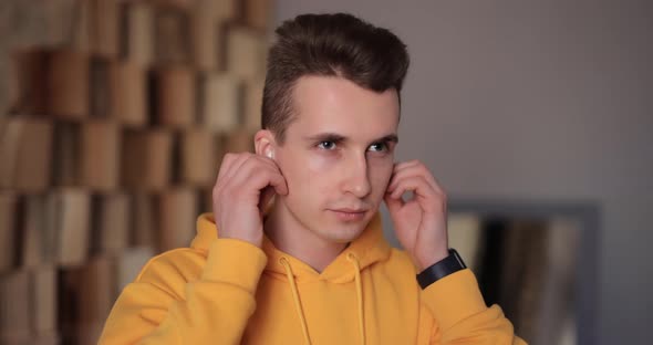 Man in Yellow Hoodie Puts on Wireless Earbuds Into His Ears at Home