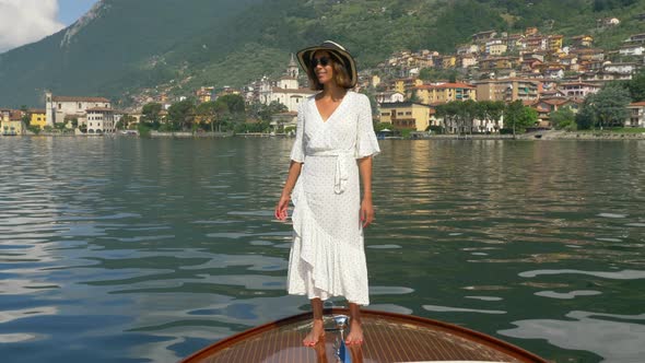 A woman standing on the bow a classic luxury wooden runabout boat on an Italian lake