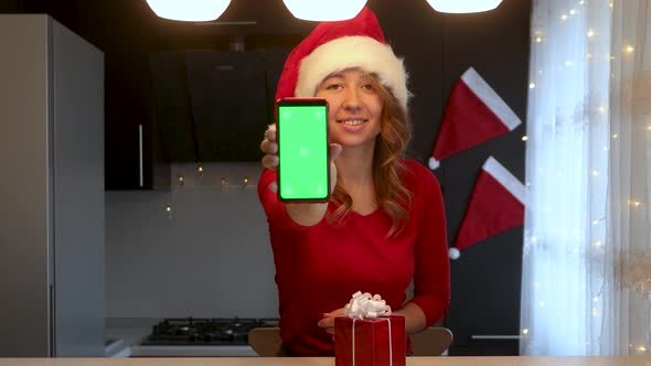 A girl in the kitchen talks by video call and shows a smartphone with a green screen