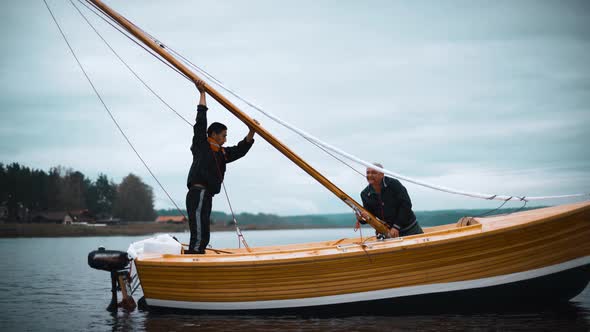 Master and His Assistant Work on Wooden Sailboat on River Try To Install Mast